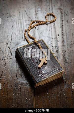 Rosenkranz mit Kreuzlegung auf altem Bibelbuch auf rustikalem Holztisch. Christentum, Religion, religiöses Symbol. Gebet. Stockfoto