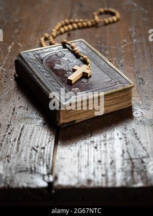 Rosenkranz mit Kreuzlegung auf altem Bibelbuch auf rustikalem Holztisch. Christentum, Religion, religiöses Symbol. Gebet. Stockfoto