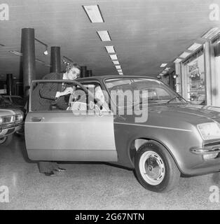 1975, historisch, in einem Autosalon, ein Verkäufer in einem Nadelstreifenanzug, der die Schlüssel und das Logbuch eines neuen Automobils, einen Vauxhall Chevette, mit einer Kundin - der neuen Besitzerin - auf dem Fahrersitz sitzt, England, Großbritannien. Der Chevette, ein kleines Familienauto, wurde zwischen 1975 und 1984 von Vauxhall Motors in Großbritannien hergestellt. Mit einem Design, das auf dem Opel Kadett basierte, war der Chevette einer der ersten in Großbritannien gebauten Heckklappen und von 1975 bis 1978 das meistverkaufte Modell Großbritanniens in dieser Klasse. Stockfoto