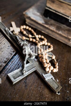 Kruzifix und Rosenkranz mit Kreuzlegen auf rustikalem Holztisch. Alte Bücher im Hintergrund. Christentum, Religion, religiöses Symbol. Gebet. Stockfoto