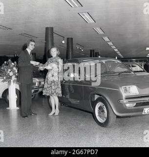 1975, historisch, in einem Autosalon, übergab ein Autoverkäufer in einem Nadelstreifenanzug das Logbuch eines neuen Automobils, eines Vauxhall Chevette, an eine glückliche Kundin, England, Großbritannien. Der Stylist Chevette, ein kleines Familienauto, wurde von Vauxhall Motors in Großbritannien zwischen 1975 und 1984 hergestellt. Mit einem Design, das auf dem Opel Kadett basierte, war der Chevette einer der ersten in Großbritannien gebauten Heckklappen und von 1975 bis 1978 das meistverkaufte Modell Großbritanniens in dieser Klasse. Stockfoto