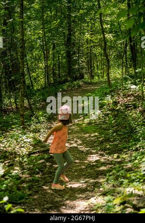 Kleines kaukasisches Mädchen, das Angst hat, dass jemand ihr in einem Wald folgt und auf dem Weg auf ihren Stalker zurückblickt Stockfoto