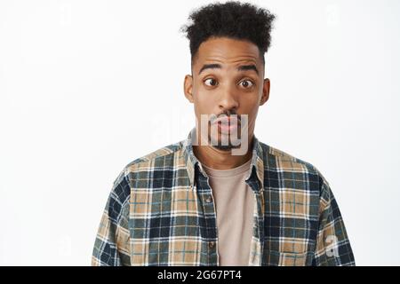 Nahaufnahme eines lustigen und albernen afroamerikanischen Mannes mit lockigem Afro-Haar, schielend, zischenden Lippen, imitierend, in legerer Kleidung dagegen stehend Stockfoto