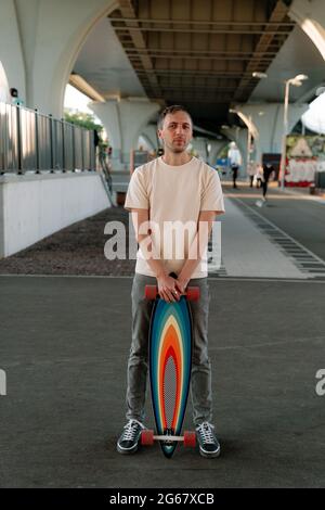 Millennial man hält Skateboard oder Longboard in Innenräumen im urbanen Raum für extreme Skating-Trainings Stockfoto