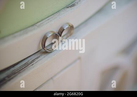 Paar Hochzeitsringe aus Weißgold mit Diamanten im Damenring. Silbernes Eheringe-Band mit Edelsteinen auf minimalistischem grauen Hintergrund mit Schattendagen Stockfoto