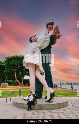 Eine Frau, die ihre amerikanische Staatsbürgerschaft feiert, vor der Statue „Embracing Peace“ eines Matrosen, der eine Krankenschwester im Tuna Harbor Park, San Diego, CA, küsst Stockfoto