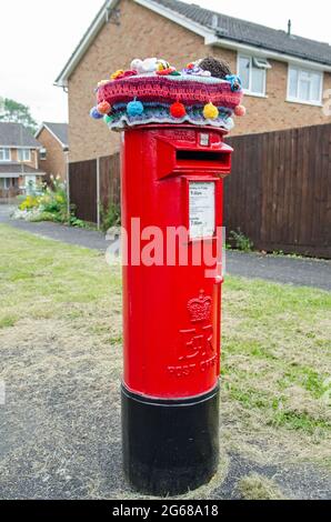 Basingstoke, Großbritannien - 3. Juli 2021: Traditionelle rote Säule der Royal Mail, gekrönt von einem gestrickten und gehäkelten Hut, komplett mit Igel, Biene und anderen Ani Stockfoto