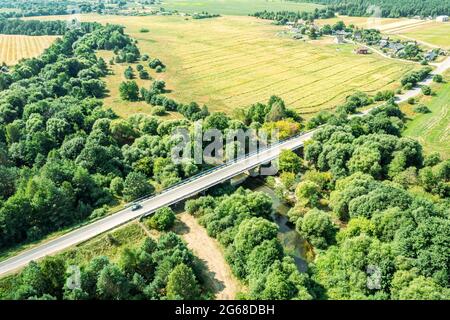 Verkehrsbrücke über einen kleinen gewundenen Fluss zwischen landwirtschaftlichen Feldern auf dem Land. Luftaufnahme Stockfoto