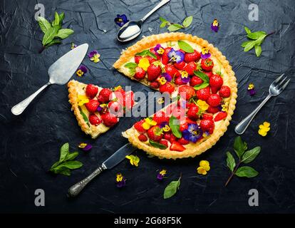 Erdbeerkuchen in Scheiben, verziert mit essbaren Blumen und Minze.Trendy Summer Berry Pie Stockfoto