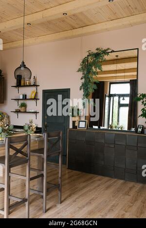 Das Interieur eines Landhauses aus Holz im skandinavischen Stil. Ein Bartisch mit Stühlen und eine Kommode mit einem großen Spiegel darüber Stockfoto