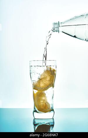 Frisches Wasser in Glas mit Zitrone aus Plastikflasche auf blauem Hintergrund gießen. Frisches Trinkwasser Glas mit Blasen blauen Hintergrund. Stockfoto