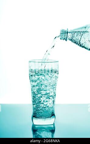 Frisches Wasser aus Plastikflasche auf blauem Hintergrund in Glas gießen. Frisches Trinkwasser Glas mit Blasen blauen Hintergrund. Stockfoto