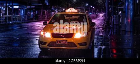 Ein gelbes Taxi in Melbourne City in einer regnerischen Nacht mit nassen Straßen und leichtem Glanz Stockfoto