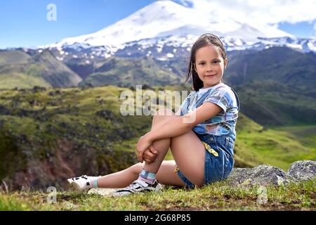 Ein kleines nettes Mädchen auf dem Hintergrund der Berggipfel. Stockfoto