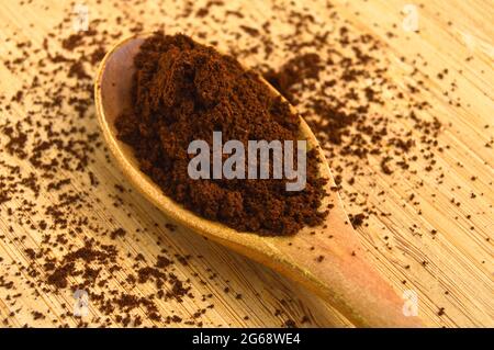 Sorgfältig ausgewählter gerösteter und pulverförmiger frischer Kaffee, Holzlöffel auf Holzboden Stockfoto