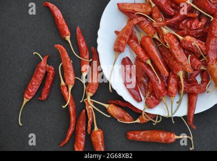 Ansicht von oben auf einem Haufen roter Chilischoten auf einem weißen Teller mit Aufstrich auf einem schwarzen Tisch mit rauer Struktur Stockfoto