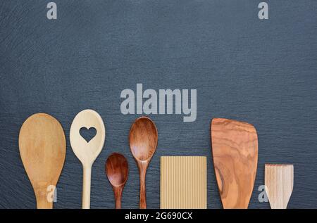 Hintergrund, Textur und Nahaufnahme einer schwarzen Schiefertafel, auf deren Unterseite verschiedene Holzlöffel nebeneinander aufgereiht sind Stockfoto