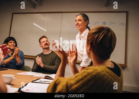 Geschäftsteam schätzt die Bemühungen des Kollegen bei der Besprechung. Geschäftsfrau, die bei Vorstandssitzungen Applaus von Kollegen bekommt. Stockfoto