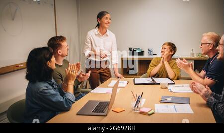 Die reife Frau applaudierte von den Kollegen, nachdem sie in der Besprechung eine Präsentation gegeben hatte. Weibliche Führungskraft wird durch das Klatschen für eine erfolgreiche Strategieplanung geschätzt. Stockfoto