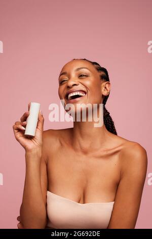 Porträt einer afrikanischen Frau, die ein Hautpflegeprodukt in der Hand hält und lächelt. Attraktive Frau mit schöner Haut hält eine kosmetische Creme-Flasche. Stockfoto