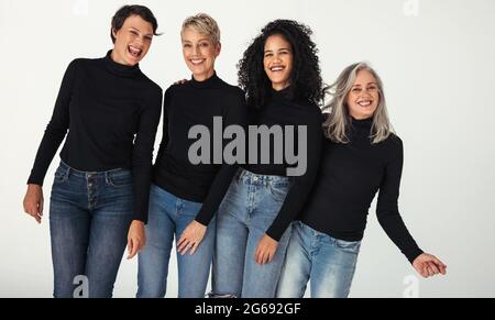 Atemberaubende Gruppe von Frauen, die ihr Alter in einem Studio feiern. Vier körperpositive Frauen unterschiedlichen Alters lächeln fröhlich, während sie Jeans tragen Stockfoto