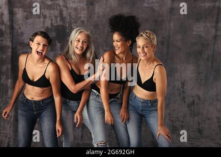 Stylische Frauen jeden Alters haben Spaß beim Tragen von Jeans und BHs. Vier körperpositive Frauen lächeln fröhlich und feiern ihre natürlichen Körper ag Stockfoto