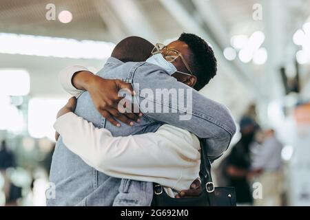 Mann umarmte Frau während einer Pandemie am Flughafenterminal. Afrikanisches Paar, das sich bei der Ankunft am Flughafen wiedervereinigt. Stockfoto