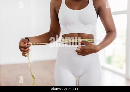 Nahaufnahme einer schwarzen Frau, die die Taille mit Klebeband misst. Schlankheitskonzept Stockfoto