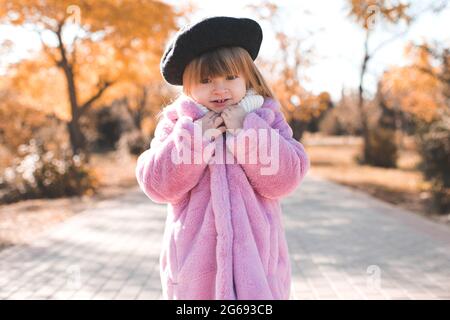 Kind Mädchen 3-4 Jahre alt tragen schwarze Baskenmütze und flauschig rosa Herbst Mantel im Park über gelben Blättern im Freien Nahaufnahme. Herbstsaison. Glück. Stockfoto