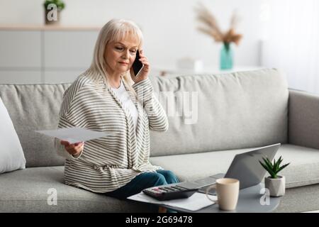 Reife Frau, die zu Hause am Handy arbeitet und spricht Stockfoto