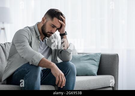 Attraktiver Kerl, der sich verzweifelt, traurig fühlt, besorgt und deprimiert nachdenklich und einsam aussieht Stockfoto