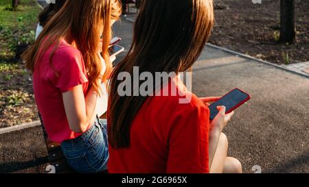 Drei Freundinnen beobachten Handys und haben Spaß auf der Bank im öffentlichen Park sitzen. Gen z, Jugendliche Geräte sucht, Digital Detox Stockfoto