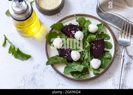 Gesunder Diätsalat mit Rucola, Spinat, Rote Beete, Mozzarella und Vinaigrette-Dressing auf einer grauen Steinplatte. Stockfoto