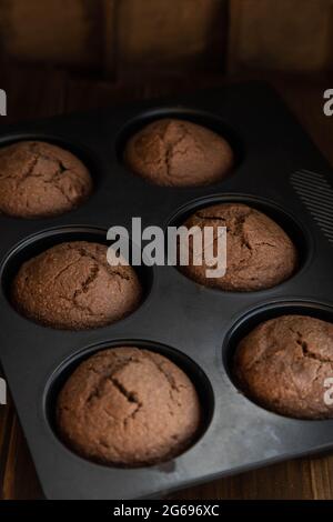 Frisch gebackene hausgemachte Schokoladen-Cupcakes in einer Kochform, stehend auf einem Holztisch. Stockfoto