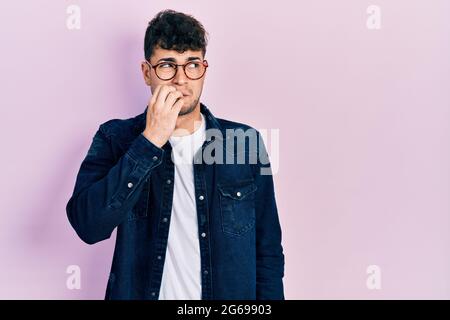 Junge hispanische Mann trägt Freizeitkleidung und Brille gestresst und nervös mit Händen auf Mund beißen Nägel. Angst Problem. Stockfoto