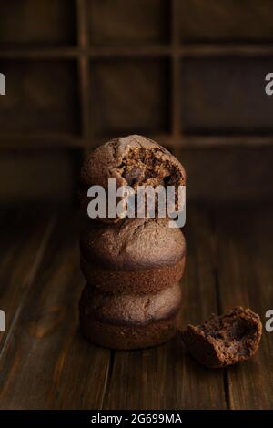 Schokolade hausgemachte Cupcakes in gestapelt, und einer von ihnen wird gebissen. Hausgemachte Brownies auf einem dunklen Holztisch in stimmungsvollen Stil. Stockfoto