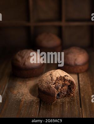 Schokolade hausgemachte Cupcakes und einer von ihnen wird gebissen. Hausgemachte Brownies auf einem dunklen Holztisch in stimmungsvollen Stil. Stockfoto