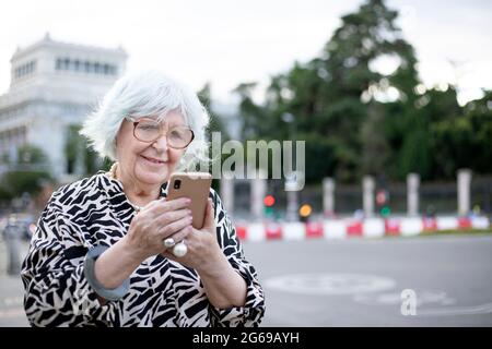 Ältere Frau, die auf der Straße mit dem Handy telefoniert Stockfoto