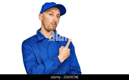 Glatze Mann mit Bart tragen Baumeister Jumpsuit Uniform zeigt mit Handfinger zur Seite Anzeige, ernst und ruhig Gesicht Stockfoto