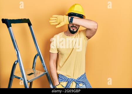 Schöner Mann mit Bart von Baustufen tragen Hardhut über Augen mit Arm, sieht ernst und traurig. Sightless, Verstecken und Ablehnung concep Stockfoto
