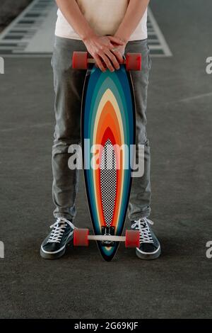 Sportlicher Mann mit hellem, farbenfrohem Longboard. Kaukasischer männlicher Hipster-Skateboarder mit Skateboard Stockfoto