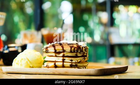 Süße Bananenpfannkuchen stapeln mit Macadamianuss und Schokoladensirup Belag auf Pfannkuchen flach legen auf Holzplatte, grünen Garten im Hintergrund verschwommen Stockfoto