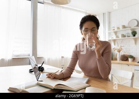 Konzentrierte junge Frau, die Glas und Wasser trinkt, Buch liest. Stockfoto