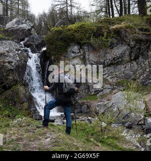Ein junger Wanderer beobachtet den kleinen Wasserfall aus kristallklarem Wasser. Stockfoto