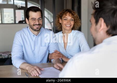 Glückliches junges Paar, das dem Manager beim Treffen im Büro zuhört Stockfoto