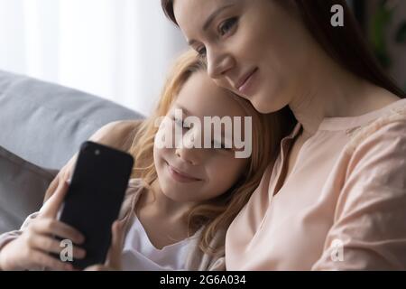 Tochter kuschelt auf der Couch mit Mama Look auf dem Telefonbildschirm Stockfoto