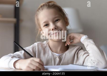 Kopfschuss Porträt lächelndes Mädchen Grundschulalter Schüler am Schreibtisch Stockfoto