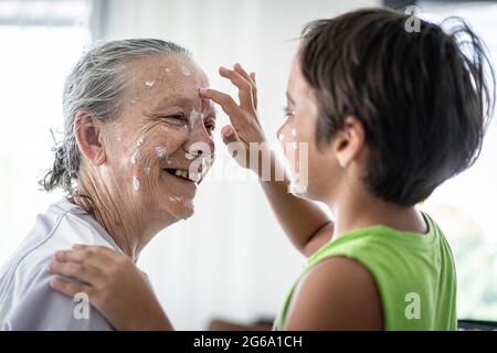 Großmutter und kleiner Junge, die Creme-Schutz auf ihr Gesicht legen Stockfoto