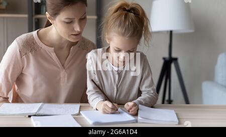Fokussierte Mutter helfen Tochter im Schulalter Hausaufgaben zu machen Stockfoto