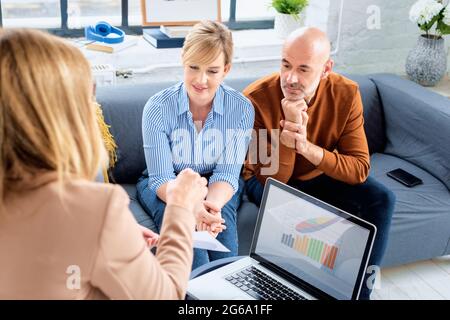 Glückliches Paar, das mit ihrem Finanzberater kommunizierte, während es zu Hause im Wohnzimmer saß. Stockfoto